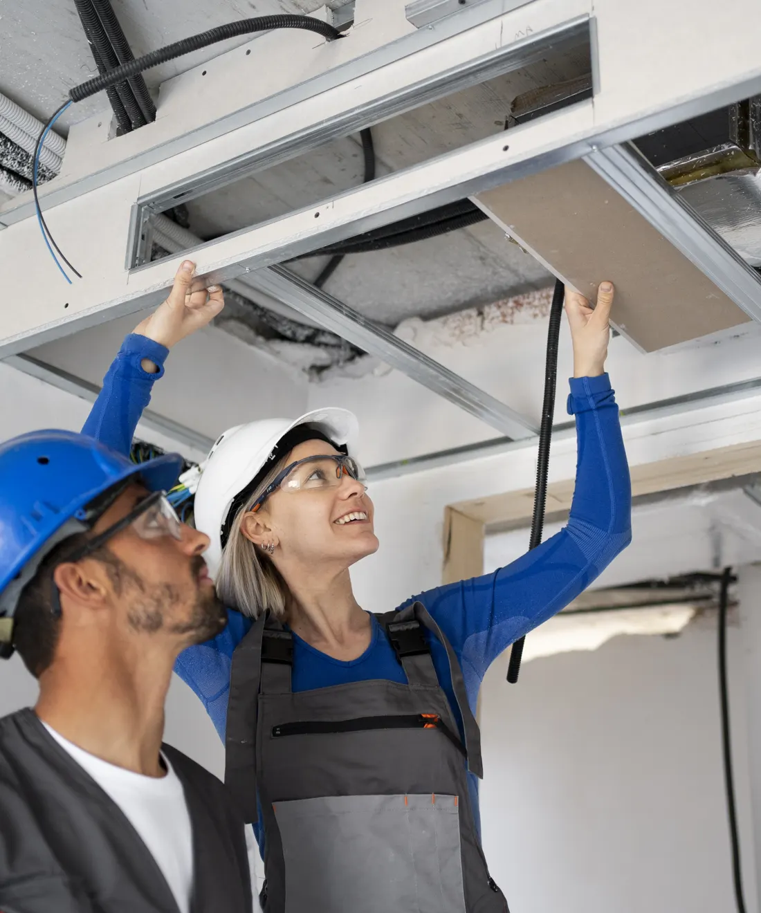 Two technicians in hard hats inspecting a ceiling air duct